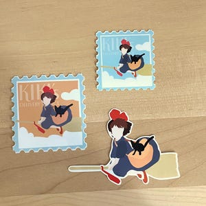 May include: Three stickers featuring a cartoon girl in a blue dress with a red bow, riding a broom with a black cat. The stickers are in the shape of postage stamps with the words "Kiki's Delivery Service". The background colors are orange and blue.