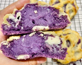 Puede incluir: Primer plano de una galleta de batata morada con chispas de chocolate blanco. La galleta está partida por la mitad, revelando el relleno de batata morada.