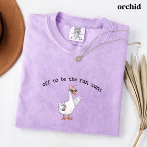 Playful goose illustration with sunglasses bow and drink printed on funny aunt themed t shirt.