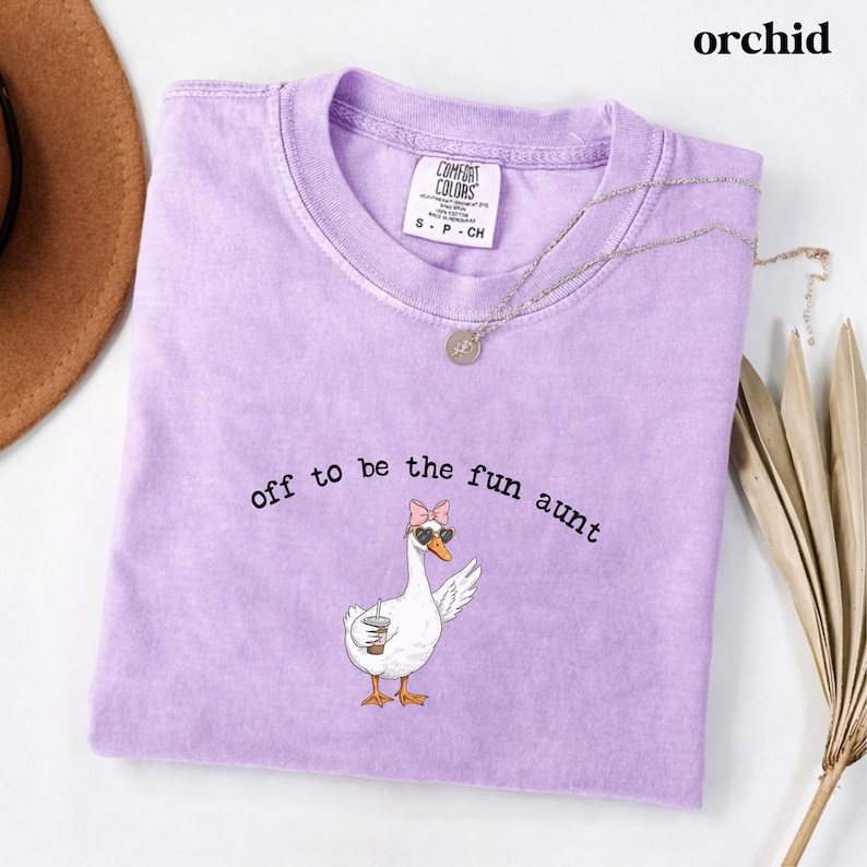 Playful goose illustration with sunglasses bow and drink printed on funny aunt themed t shirt.