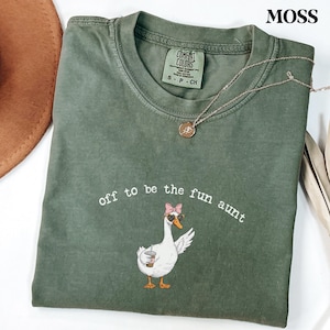 Cute goose graphic wearing sunglasses and pink bow with drink in wing printed on comfort colors style shirt.