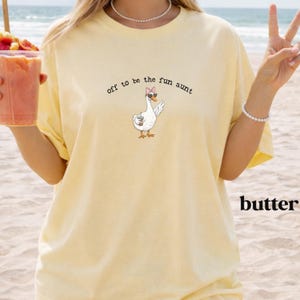 Playful goose wearing sunglasses and bow holding beverage printed on casual aunt shirt.