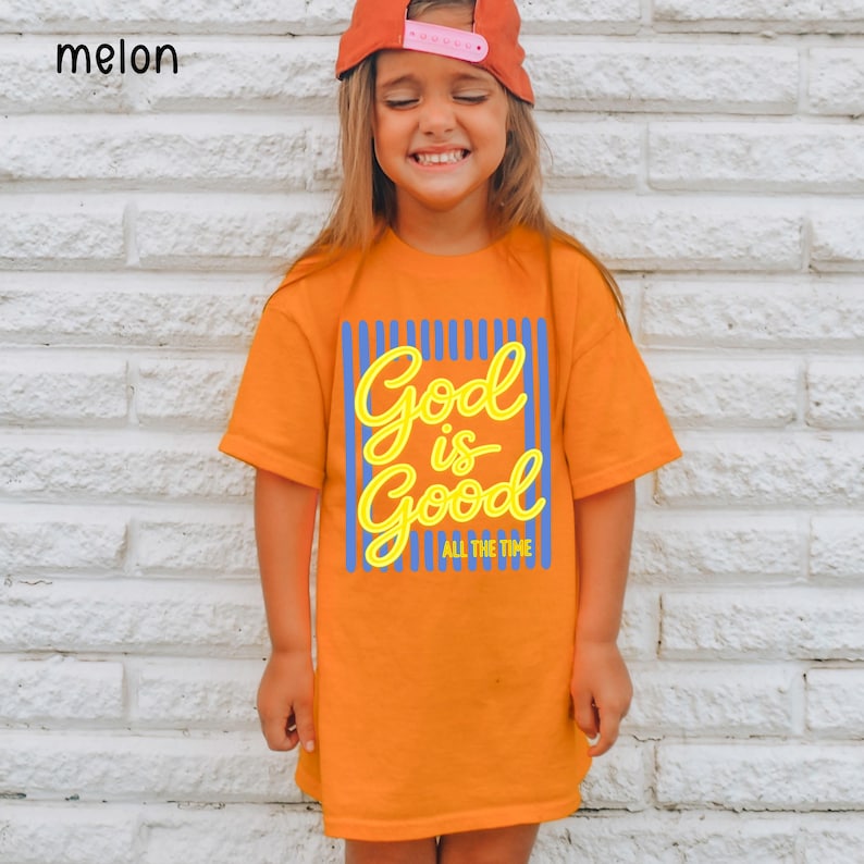 May include: An orange short-sleeved t-shirt featuring a graphic print with vertical blue stripes and the yellow text God is Good ALL THE TIME. The shirt has a crew neckline and a straight hem, providing a simple and classic fit for casual wear.