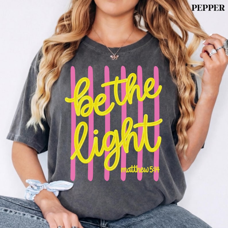 Minimalist Christian shirt with bright Be the Light lettering.