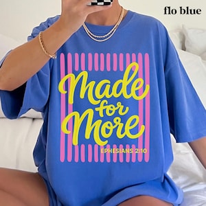 May include: A blue t-shirt with the words "Made for More" in yellow script, framed by pink vertical lines. The text "Ephesians 2:10" is below the main text. The shirt is labeled "flo blue" in the upper right corner.