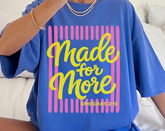 May include: A blue t-shirt with the words "Made for More" in yellow script, framed by pink vertical lines. The text "Ephesians 2:10" is below the main text. The shirt is labeled "flo blue" in the upper right corner.