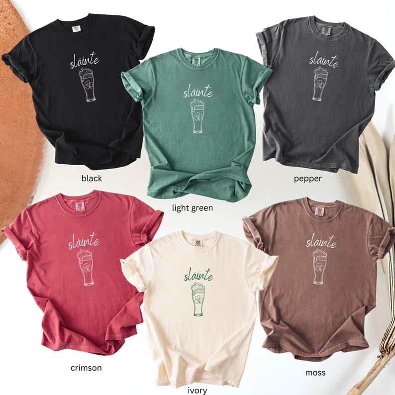 May include: Six short-sleeved t-shirts in various colors: black, light green, pepper, crimson, ivory, and moss. Each shirt features the word "slainte" above a beer glass illustration. The shirts are made of a soft material.