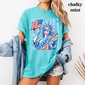 Patriotic women and kids tee with retro Statue of Liberty America design.
USA America shirt featuring bubble gum Statue of Liberty and hot dog artwork.
250th anniversary patriotic shirt with Statue of Liberty and American flag graphi