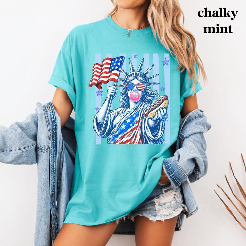 Patriotic women and kids tee with retro Statue of Liberty America design.
USA America shirt featuring bubble gum Statue of Liberty and hot dog artwork.
250th anniversary patriotic shirt with Statue of Liberty and American flag graphi