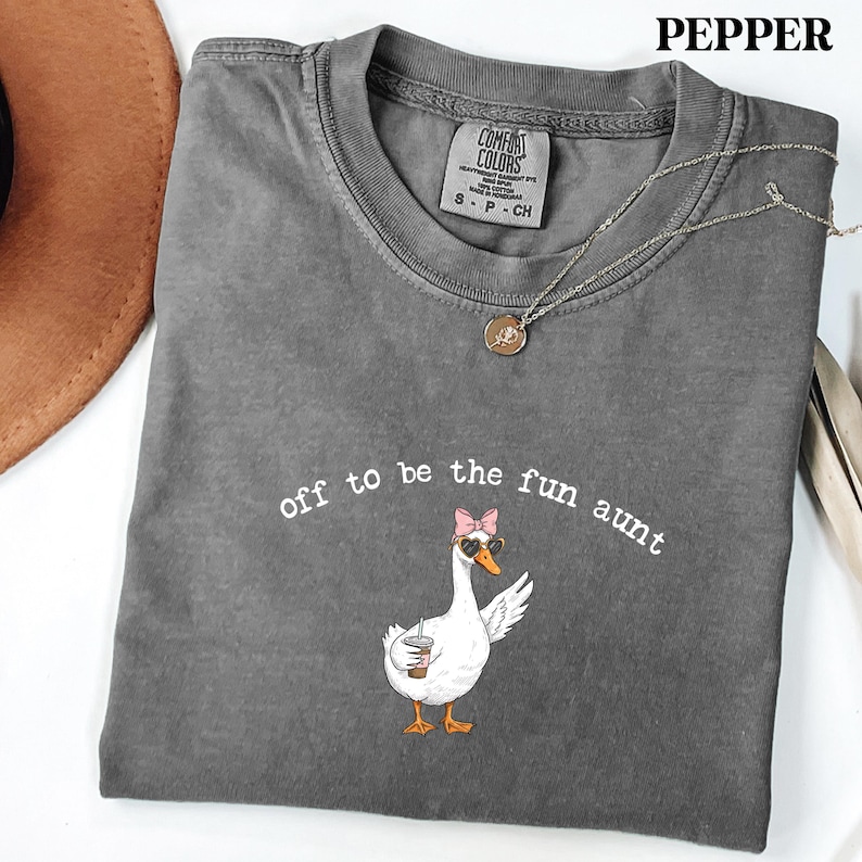 Trendy goose character with sunglasses and bow holding beverage printed on casual graphic apparel.
