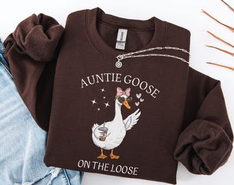 May include: Dark chocolate-colored sweatshirt with the text "AUNTIE GOOSE ON THE LOOSE" and a cartoon goose wearing sunglasses and a pink bow. A silver necklace is draped across the sweatshirt. The words "DARK CHOCOLATE" are in the upper left corner.