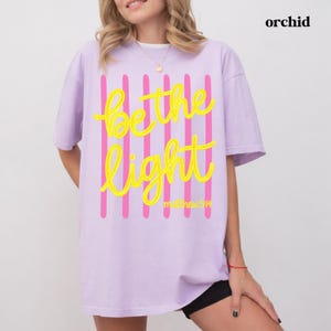 Christian graphic tee with Be the Light scripture inspired artwork.