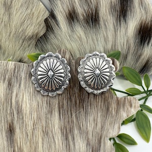 May include: A pair of silver earrings with a geometric design. The earrings are round and have a raised center with a diamond shape.