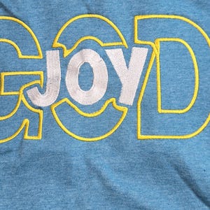 May include: A blue t-shirt with the words "GOD" and "JOY" embroidered in yellow on the front.