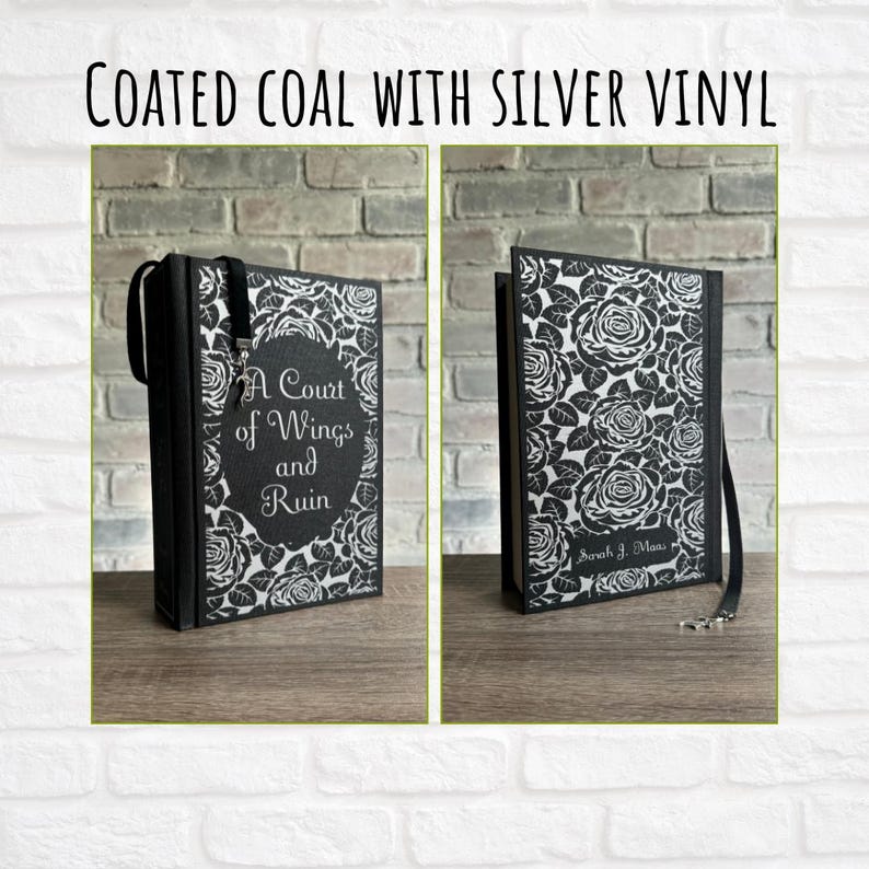 May include: A black book cover with a silver floral design and the title "A Court of Wings and Ruin." The book has a black ribbon bookmark and a silver clasp. The text "Coated Coal with Silver Vinyl" is at the top.