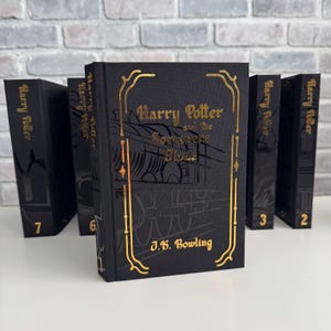 May include: A set of black hardback books with gold lettering. The front book is titled "Harry Potter and the Sorcerer's Stone" by J.K. Rowling. The spines of the books are labelled "Harry Potter" and numbered.