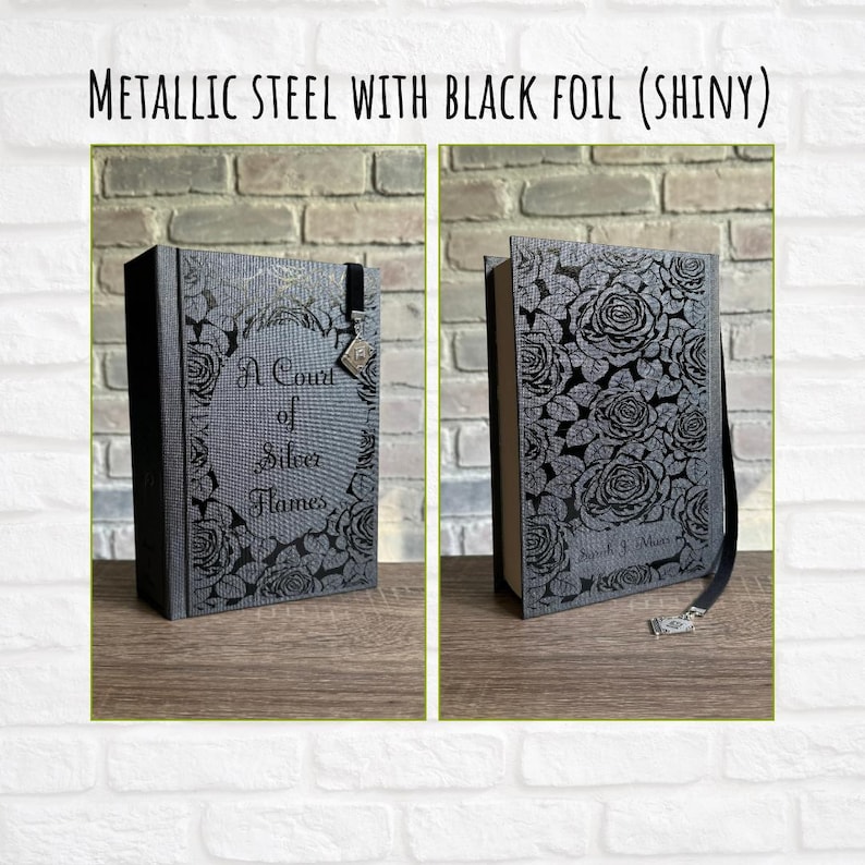 May include: Two views of a book with a metallic steel cover and black foil floral design. The book's title is "A Court of Silver Flames." The cover features a decorative clasp and a black ribbon bookmark.