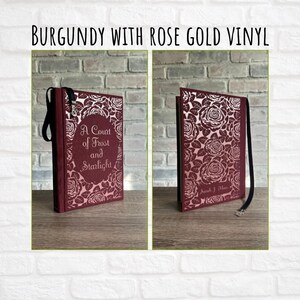 May include: Burgundy journal with rose gold vinyl. The journal features a floral rose design and the text "A Court of Frost and Starlight." A black ribbon is attached to the spine. The cover is burgundy.