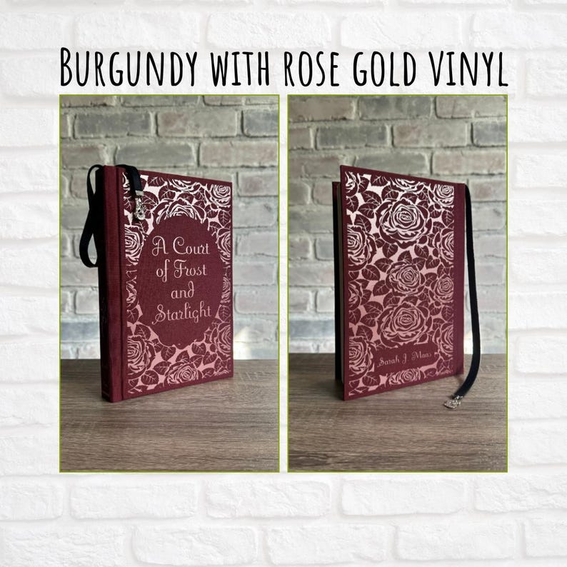 May include: Burgundy journal with rose gold vinyl. The journal features a floral rose design and the text "A Court of Frost and Starlight." A black ribbon is attached to the spine. The cover is burgundy.