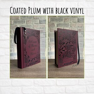 May include: Coated plum book with black vinyl featuring the text "A Court of Thorns and Roses" and a floral design. The book has a black ribbon bookmark with a silver charm.