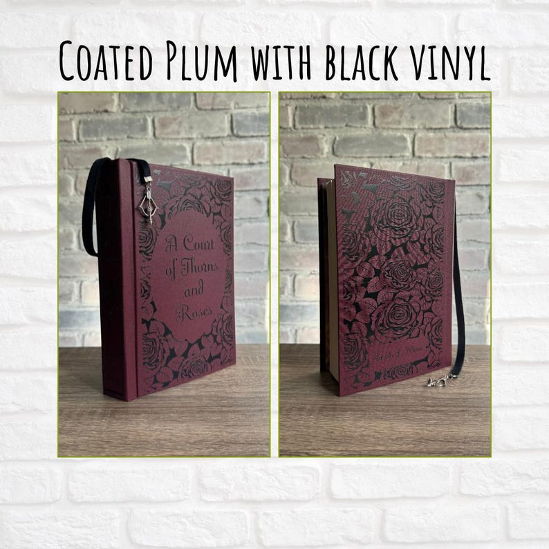 May include: Coated plum book with black vinyl featuring the text "A Court of Thorns and Roses" and a floral design. The book has a black ribbon bookmark with a silver charm.