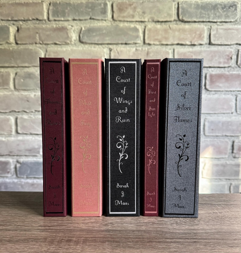 May include: A collection of six hardcover books with matching spines. The books are in various colors, including burgundy, coral, black, and gray. Each book features the title and author's name in white text, with an elegant floral design.