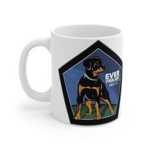 May include: White ceramic mug with a black and green pentagon design. Inside the pentagon is a black and brown dog with a green collar. The text "EVER VIGILANT" and "NRL-45" are printed in white inside the pentagon.