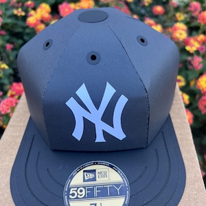 May include: Black and white New Era 59FIFTY fitted baseball cap with a New York Yankees logo. The cap has a black brim and a black crown with a black sticker on the top. The sticker says "New Era" and "59FIFTY". The size of the cap is 7 1/4, which is 57.7cm.