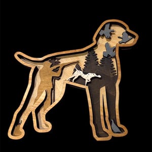 May include: A layered wooden art piece in the shape of a dog, featuring a hunter, trees, and birds. The dog silhouette is crafted from light and dark wood tones, with a black background. A smaller dog with spots is also included.