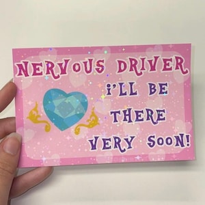 Puede incluir: Una pegatina rectangular rosa con acabado hologr&aacute;fico, decorada con corazones y estrellas blancas. El texto NERVOUS DRIVER I'LL BE THERE VERY SOON! aparece en letras moradas. Incluye un coraz&oacute;n azul facetado con adornos dorados.