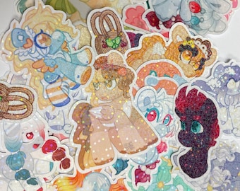 Puede incluir: Una colección de pegatinas brillantes y coloridas con animales y personajes de dibujos animados. Las pegatinas están sobre un fondo blanco y tienen una variedad de diseños, incluyendo un unicornio, un gato, un perro y un pájaro.
