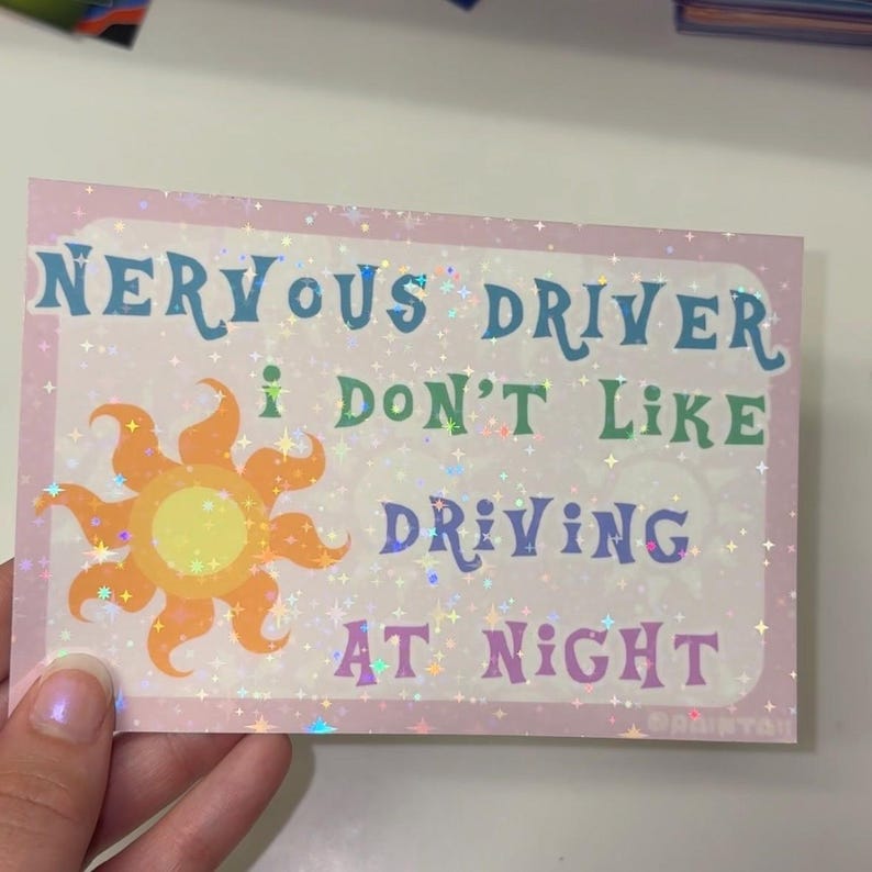 Puede incluir: Una pegatina rectangular con acabado hologr&aacute;fico de estrellas sobre un fondo rosa claro. Presenta un gr&aacute;fico de sol amarillo y naranja y el texto: NERVOUS DRIVER I DON'T LIKE DRIVING AT NIGHT en letras azules, verdes y moradas.