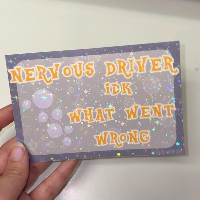 Puede incluir: Una pegatina rectangular con fondo morado oscuro que presenta un patr&oacute;n hologr&aacute;fico de estrellas y burbujas. El texto dice en letras naranjas con borde blanco: NERVOUS DRIVER IDK WHAT WENT WRONG. La pegatina tiene un acabado brillante.