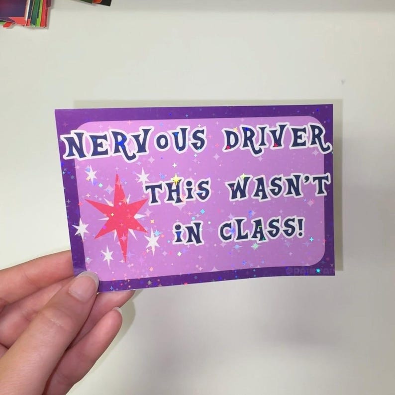 Pu&ograve; includere: Un adesivo rettangolare con sfondo viola e un motivo a stelle olografiche. Il testo "NERVOUS DRIVER THIS WASN'T IN CLASS!" &egrave; scritto in lettere blu scuro. Una grande stella rossa e diverse stelle bianche pi&ugrave; piccole sono stampate a sinistra.