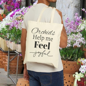 Eine Canvas-Einkaufstasche mit der Aufschrift „Orchids Help me Feel Joyful“ mit Cattleya-Blüten und „Orchid Oasis under construction“ ist das perfekte Geschenk für Pflanzenliebhaber