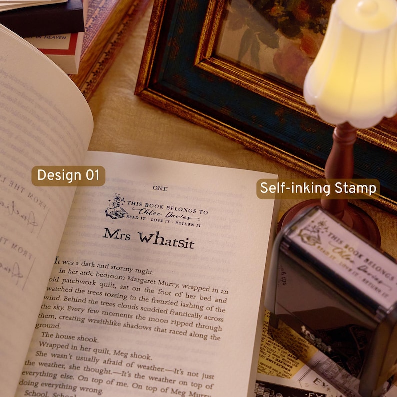 May include: A self-inking stamp featuring the text 'THIS BOOK BELONGS TO Chloe Davies READ IT LOVE IT RETURN IT' with a floral book icon. The stamp is shown next to an open book displaying the same design printed on the page, with text labels Design 01.