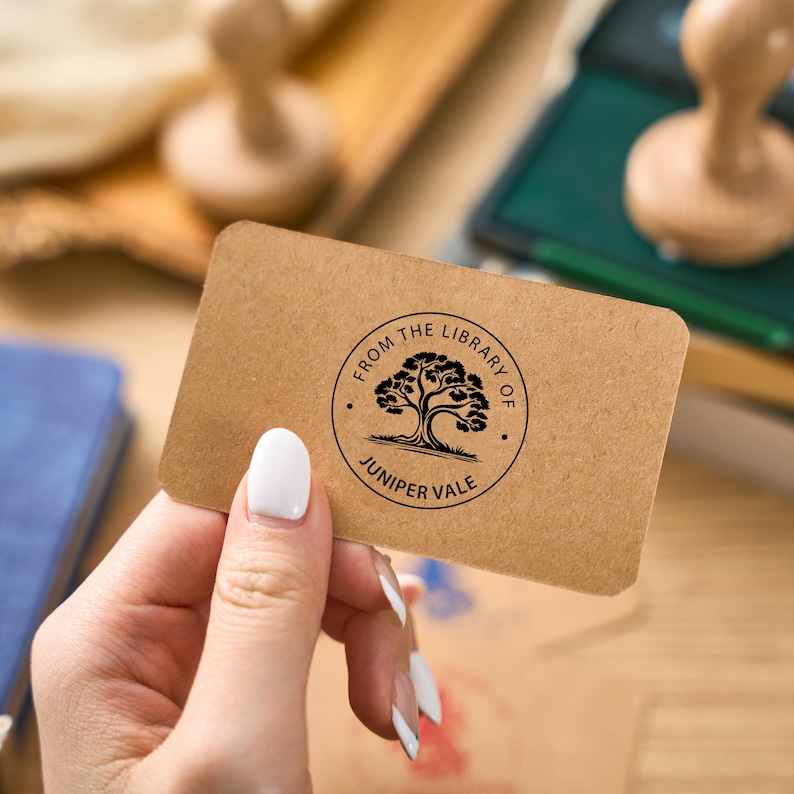 May include: A brown card with a black and white stamp that reads "From the Library of Juniper Vale". The stamp features a tree with a thick trunk and branches.