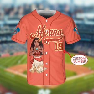 Pu&ograve; includere: Maglia da baseball color corallo con la scritta "Moana" in corsivo, il numero 19 e un'illustrazione di Moana. La maglia ha una chiusura a bottoni sul davanti e maniche corte. Il testo "Custom Number" &egrave; visibile.
