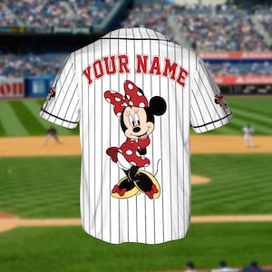 May include: White baseball jersey with black vertical stripes, featuring a Minnie Mouse graphic on the back. The jersey has the text "YOUR NAME" in red arched across the upper back. Minnie Mouse is wearing a red polka dot dress and bow.
