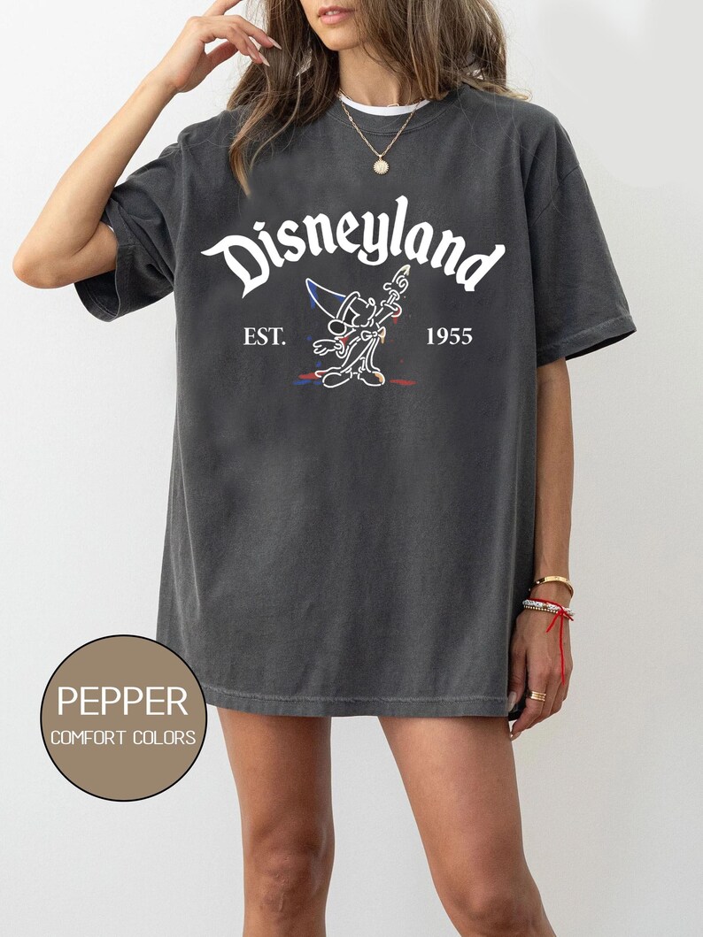 May include: A dark gray t-shirt with a white graphic of Mickey Mouse as a sorcerer, with the text "Disneyland" above and "EST. 1955" below.