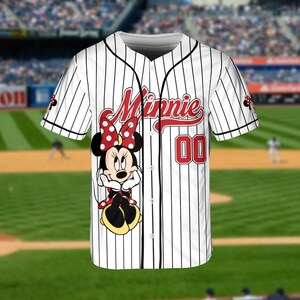 May include: White baseball jersey with black pinstripes, featuring a Minnie Mouse graphic. The jersey has the word "Minnie" in red script and the number "00" on the front. The sleeves have a Minnie Mouse design.