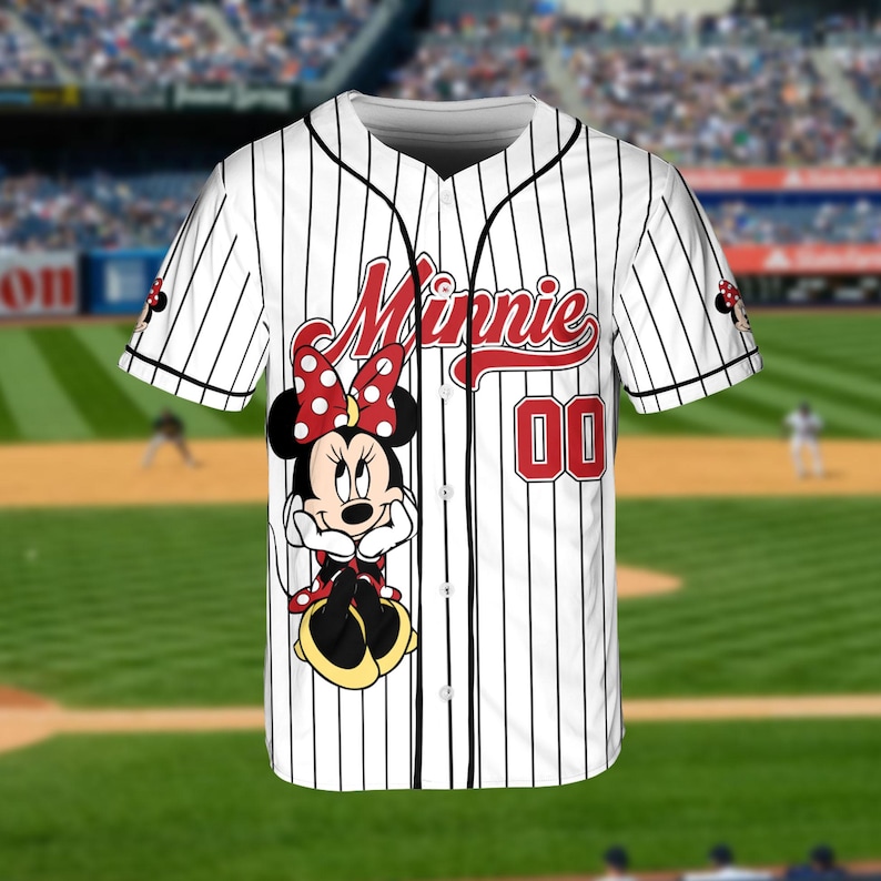May include: White baseball jersey with black pinstripes, featuring a Minnie Mouse graphic. The jersey has the word "Minnie" in red script and the number "00" on the front. The sleeves have a Minnie Mouse design.