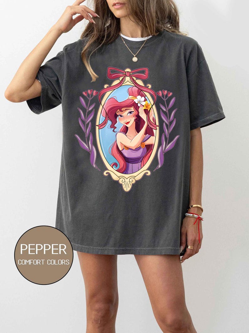 May include: A dark gray oversized t-shirt with a graphic print of a cartoon woman with long red hair in a purple dress. The woman is holding a flower in her hair. The graphic is framed in a gold oval with a purple ribbon.