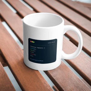 Könnte beinhalten: Weiße Keramiktasse mit einem dunkelblauen Rechteck mit Programmcode und dem Text "Coding_Life.txt". Die Tasse hat einen gebogenen Henkel und steht auf einer Holzoberfläche.