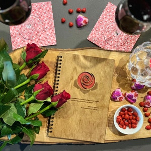 May include: A wooden journal with a spiral binding and a rose design on the cover. The journal is surrounded by red roses, red and pink heart-shaped chocolates, and a lit candle in a glass holder. The text on the journal reads "I give you my heart, for it is yours to keep.  For it is a Rose, for my love is true."