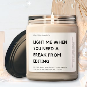 May include: A beige candle in a glass jar with a silver lid. The candle has a label that reads "Light me when you need a break from editing.  Infused with a hint of appreciation and a whole lot of gratitude."