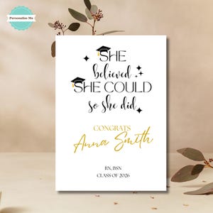 May include: A white graduation announcement with black and gold text. The text reads "She believed she could so she did" with the name "Anna Smith" in gold. Includes "RN, BSN CLASS OF 2026". Features graduation cap illustrations.