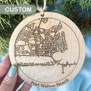 May include: A wooden ornament with a laser-engraved map of Fort Walton Beach, Florida. The ornament is round and has a natural wood finish. The text "CUSTOM" is visible in the top left corner of the image.