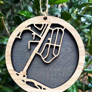 May include: A wooden ornament shaped like a city map with a dark brown background. The ornament is hanging from a twine string.