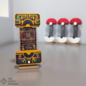 May include: A black and gold Pokemon card display stand with a holographic Pokemon card featuring a Meowth illustration. The stand has a clear plastic window to display the card. Three red and white Pokeball stands are in the background.